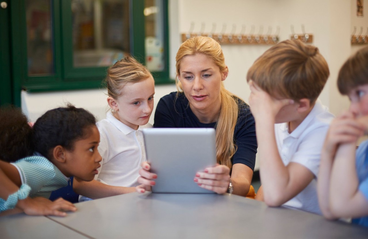Teacher holding a tablet device with students in a school