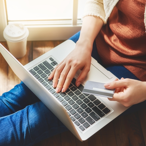 A woman sitting on floor making a payment on laptop